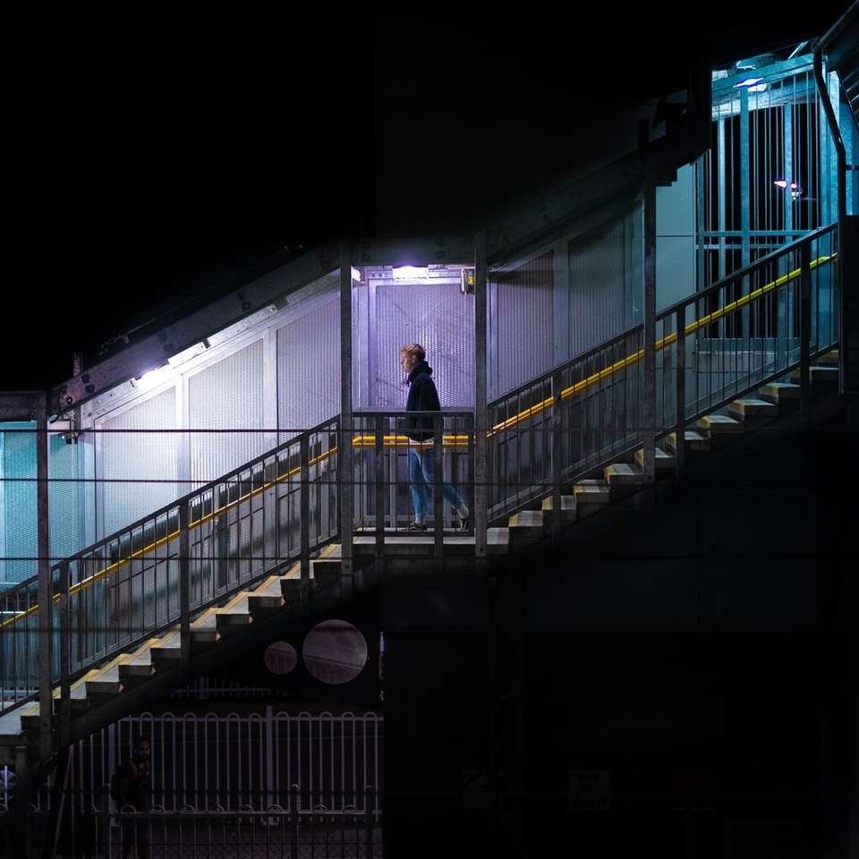 мъж в черно яке, стоящ на черен метален мост плъзгащ се пъзел онлайн
