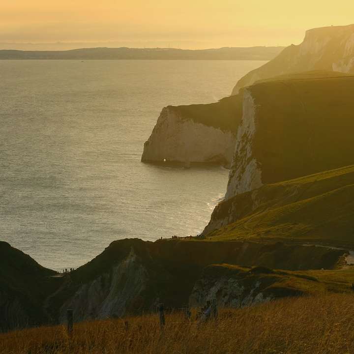Montaña verde y marrón al lado del mar durante el día rompecabezas en línea