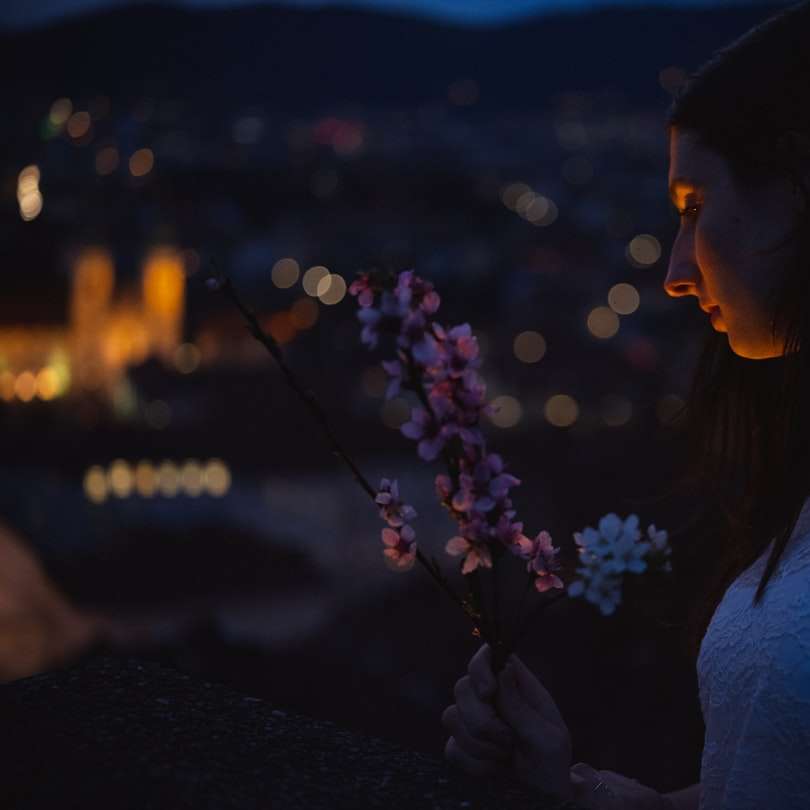 donna in camicia bianca che tiene un fiore viola durante la notte puzzle online