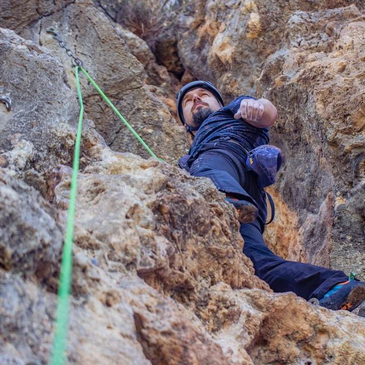 persoon in blauwe jas die op bruine rotsberg klimt schuifpuzzel online