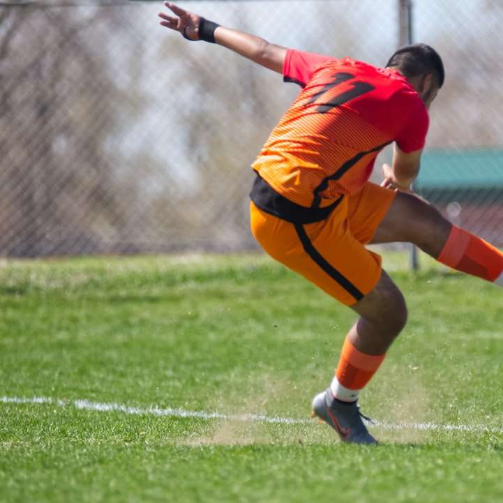 Мужчина в оранжевой майке пинает футбольный мяч онлайн-пазл