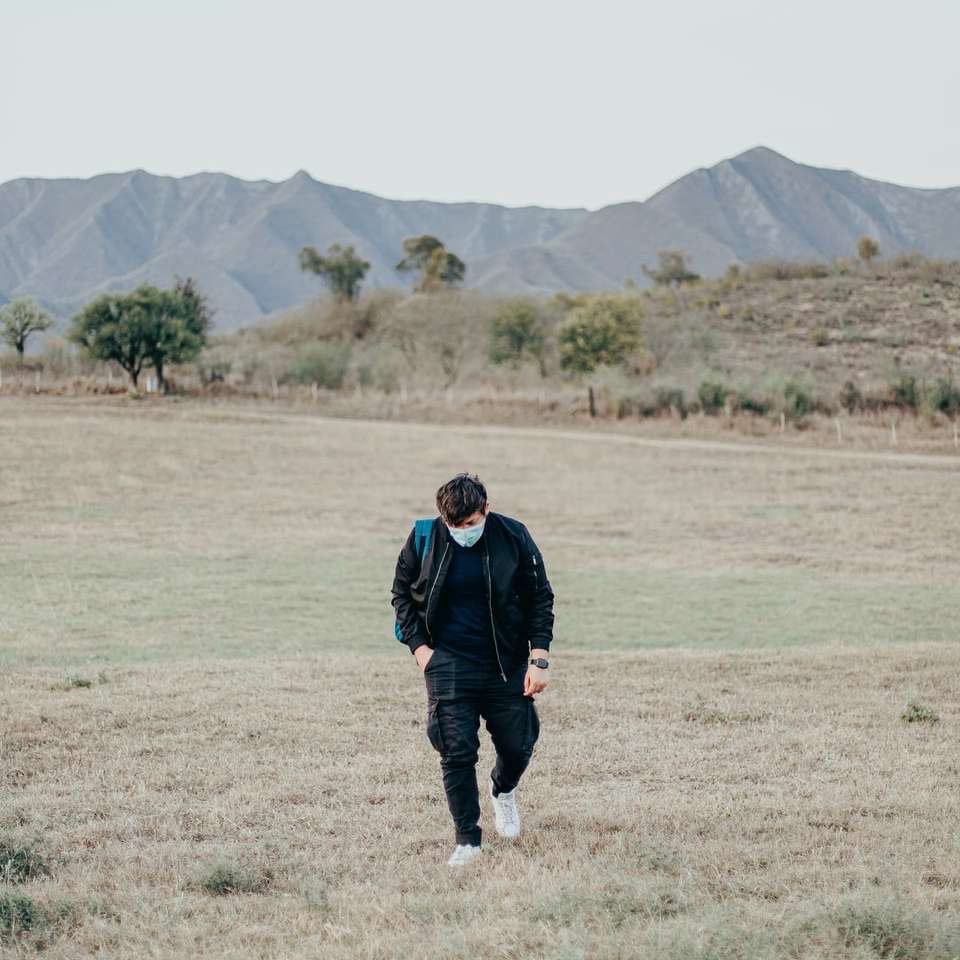 человек в черной куртке гуляет по зеленой траве онлайн-пазл