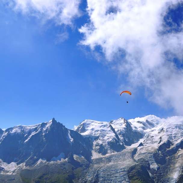 Persona en paracaídas naranja sobre montaña cubierta de nieve rompecabezas en línea