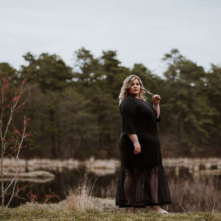 kobieta w czarnej sukience z długim rękawem stojąca na polu trawy puzzle przesuwne online