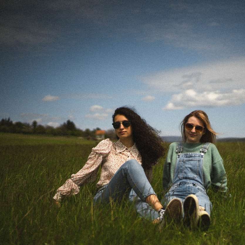 2 γυναίκες που κάθονται στο πράσινο γρασίδι κάτω από το γαλάζιο του ουρανού συρόμενο παζλ online