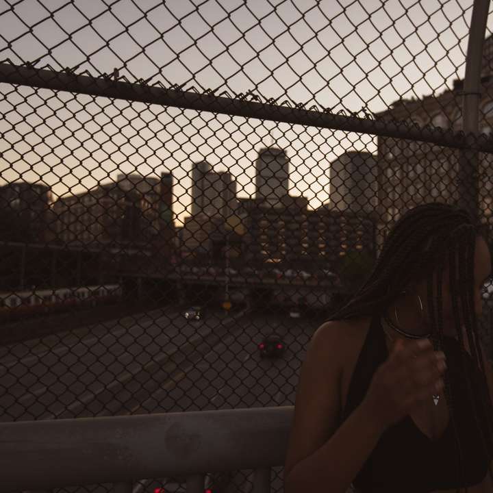 Femme en débardeur noir s'appuyant sur une clôture en métal gris puzzle coulissant en ligne