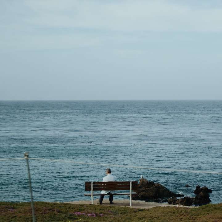 persona seduta su una panca di legno bianca vicino al mare durante il giorno puzzle online