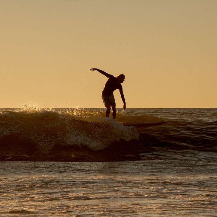 man i svarta shorts surfar på havet under dagtid glidande pussel online