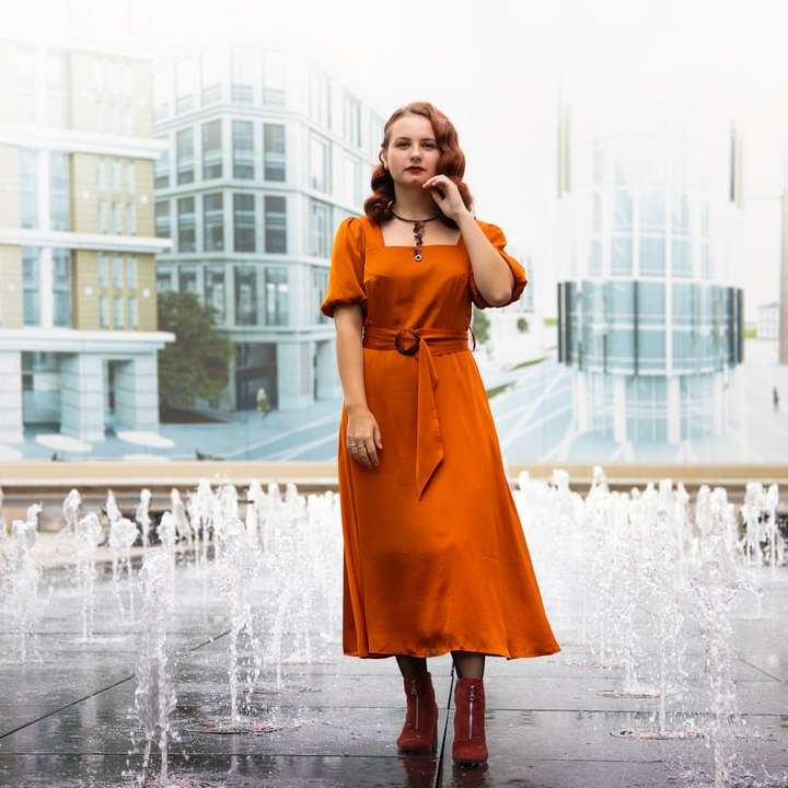 žena v oranžových šatech stojící na vodní fontáně online puzzle