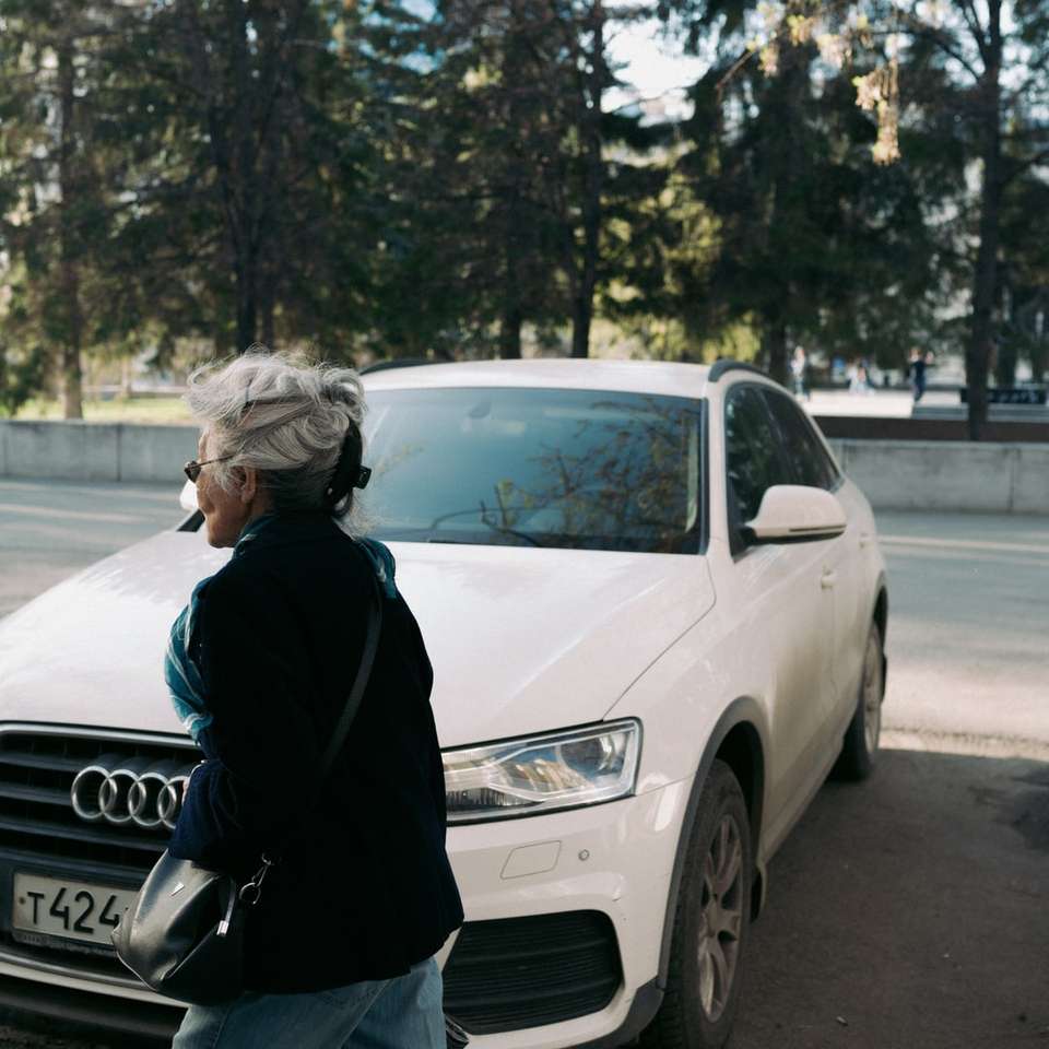 Mujer en chaqueta negra de pie junto a un coche audi blanco rompecabezas en línea