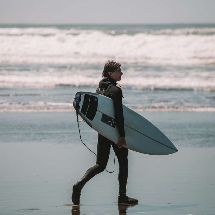 kobieta w czarno-białym kombinezonie trzymająca białą deskę surfingową puzzle przesuwne online