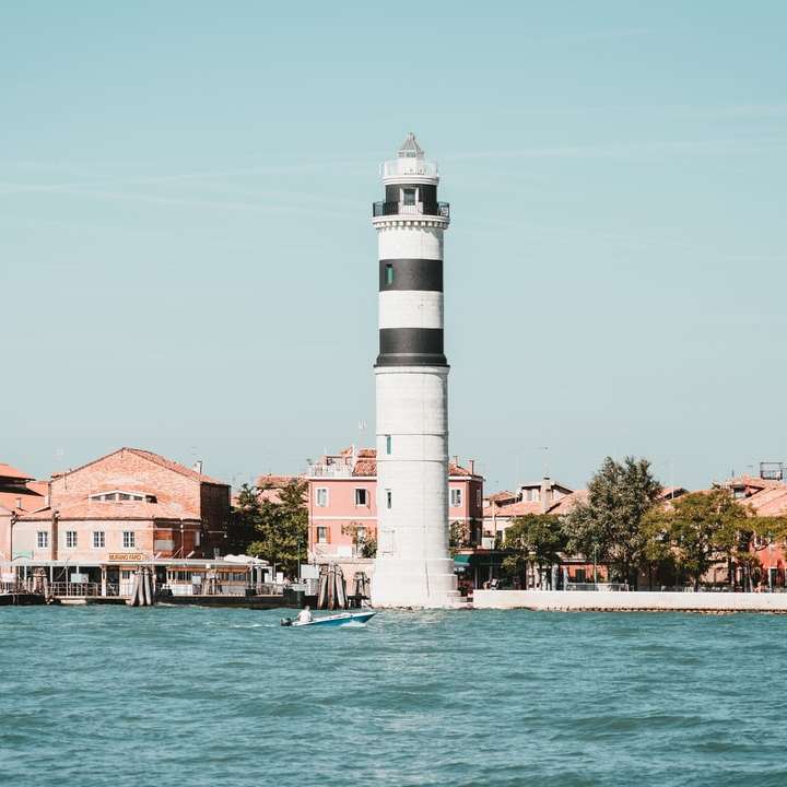 white lighthouse near houses and body of water sliding puzzle online