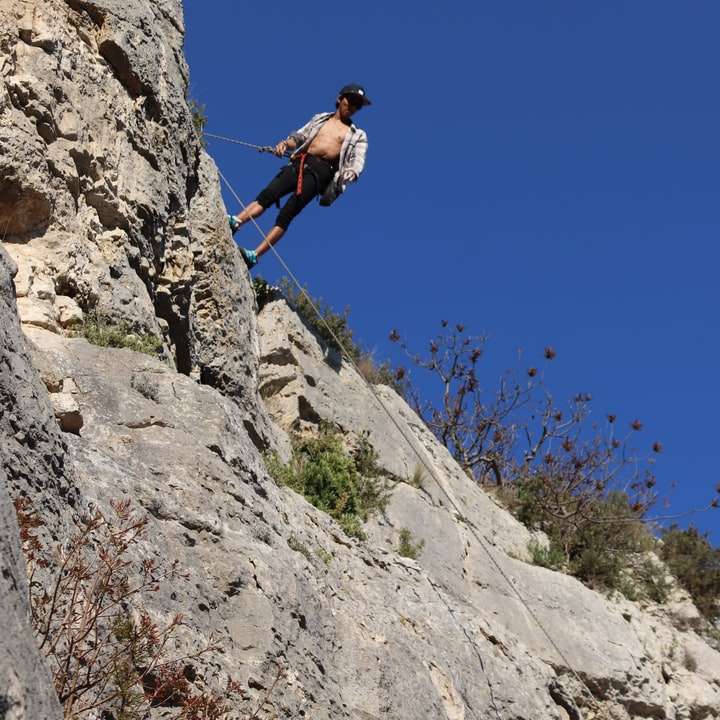 férfi kék kabátban mászik a sziklás hegyen napközben online puzzle