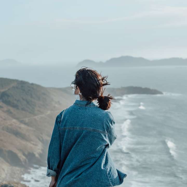 kobieta w niebieskiej dżinsowej kurtce stojąca na klifie w ciągu dnia puzzle przesuwne online