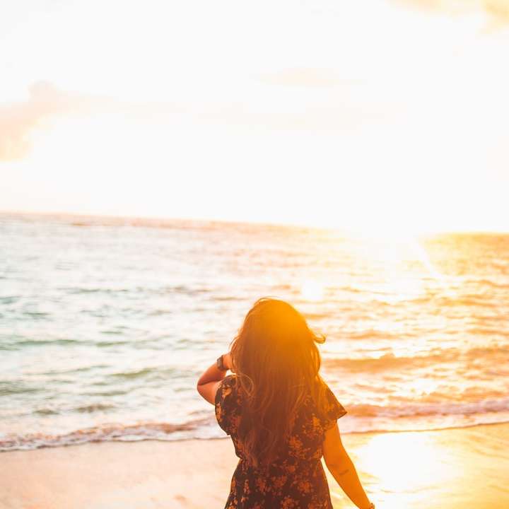 donna in abito floreale nero e marrone in piedi sulla riva del mare puzzle scorrevole online