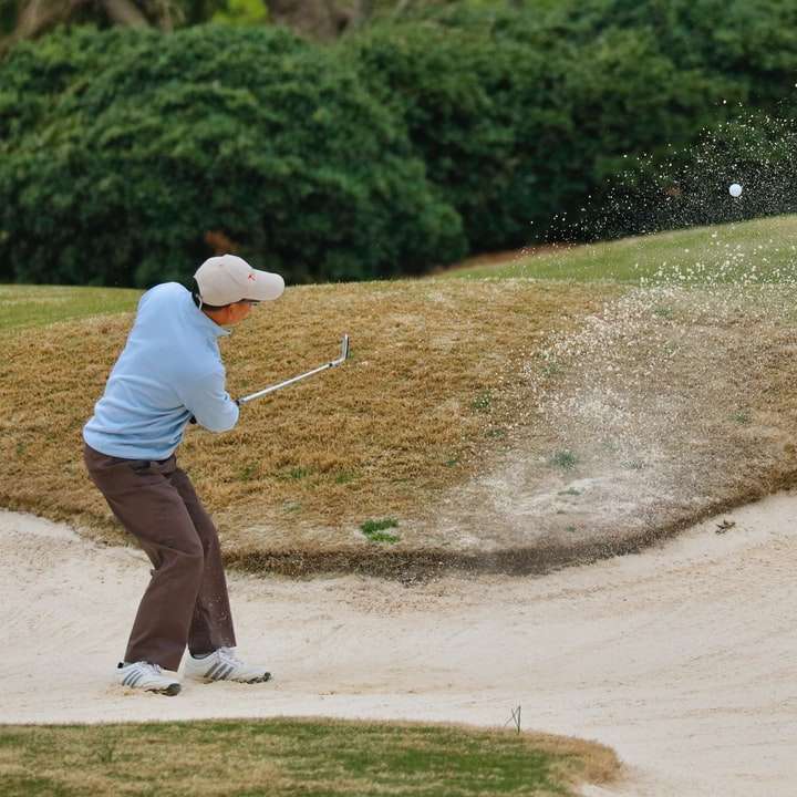 човек с бяла риза и кафяви панталони, който държи стик за голф плъзгащ се пъзел онлайн