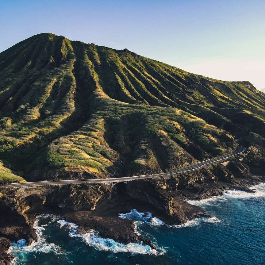 Montanha verde e marrom ao lado do mar durante o dia puzzle online