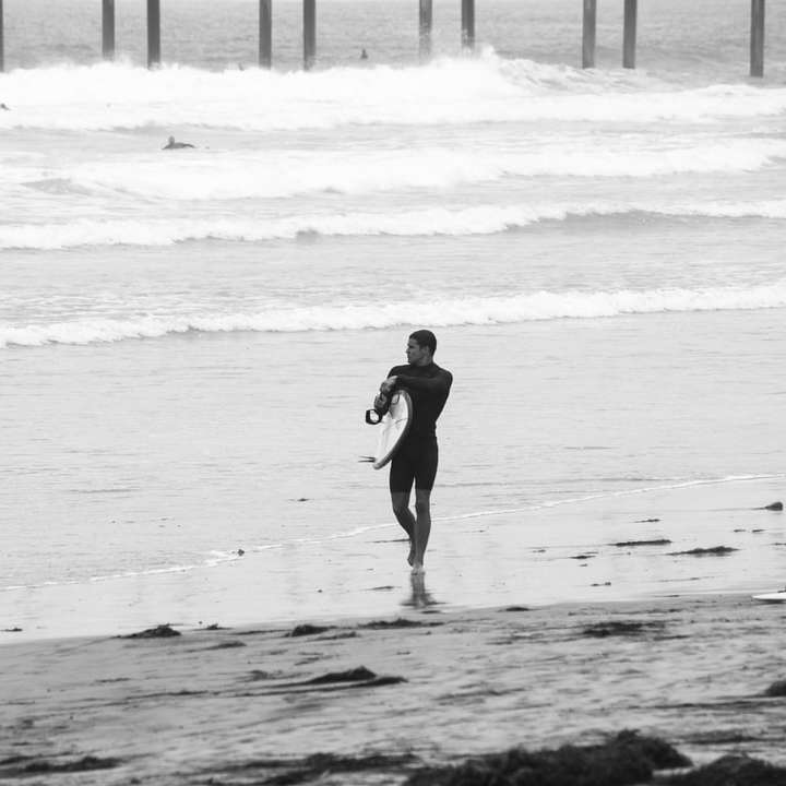 man i svart våtdräkt som går på stranden under dagtid Pussel online