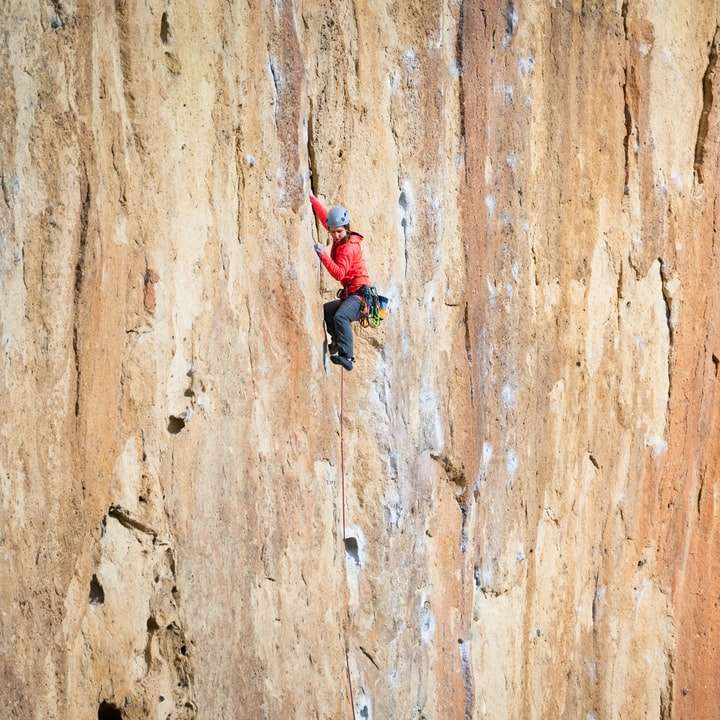 Mujer de chaqueta roja y pantalón negro escalada en la pared marrón puzzle deslizante online
