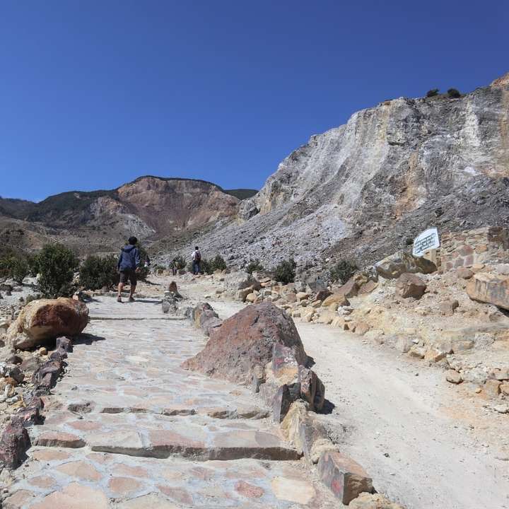 ludzie chodzą po kamienistej drodze w pobliżu skalistej góry puzzle przesuwne online