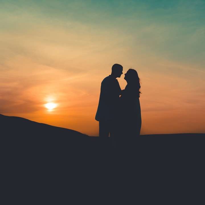 日没時に丘の上に立っているカップルのシルエット スライディングパズル・オンライン