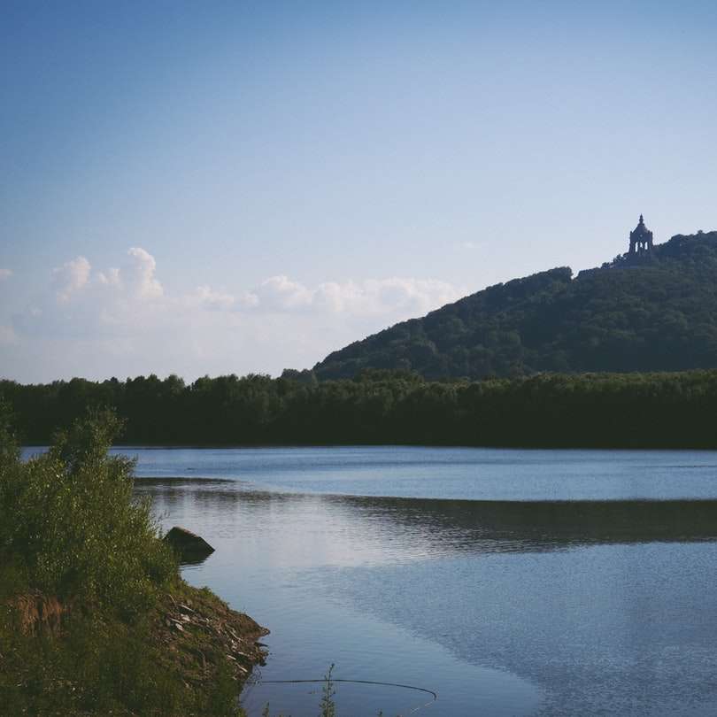 grönt berg vid sjön under blå himmel under dagtid Pussel online
