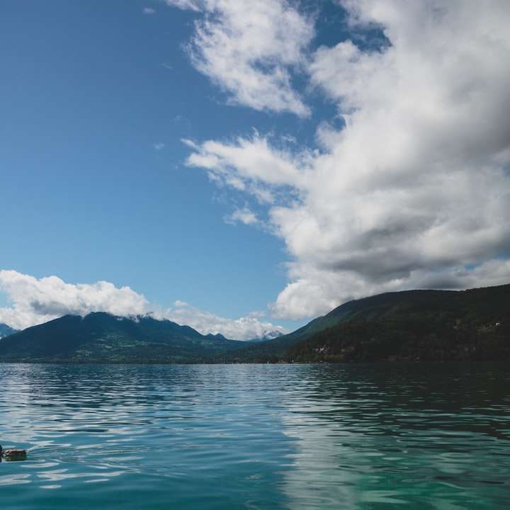persona en barco en el mar cerca de la montaña bajo un cielo azul rompecabezas en línea