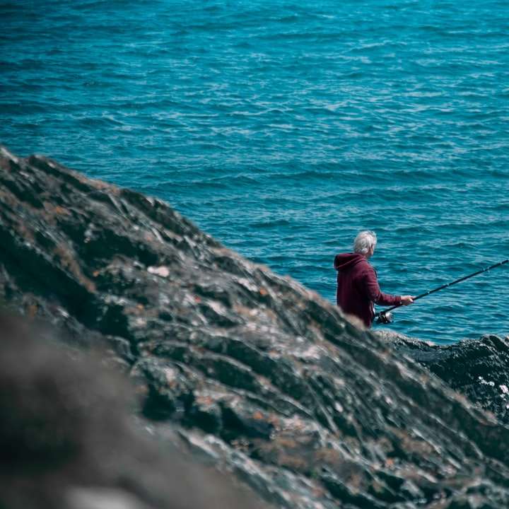 Person in roter Jacke und schwarzer Hose sitzt auf Felsen Schiebepuzzle online
