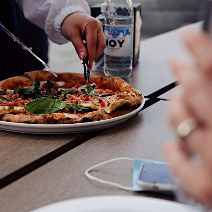 άτομο που κρατά μπλε και μαύρα ξυλάκια κόβει την πίτσα σε φέτες online παζλ