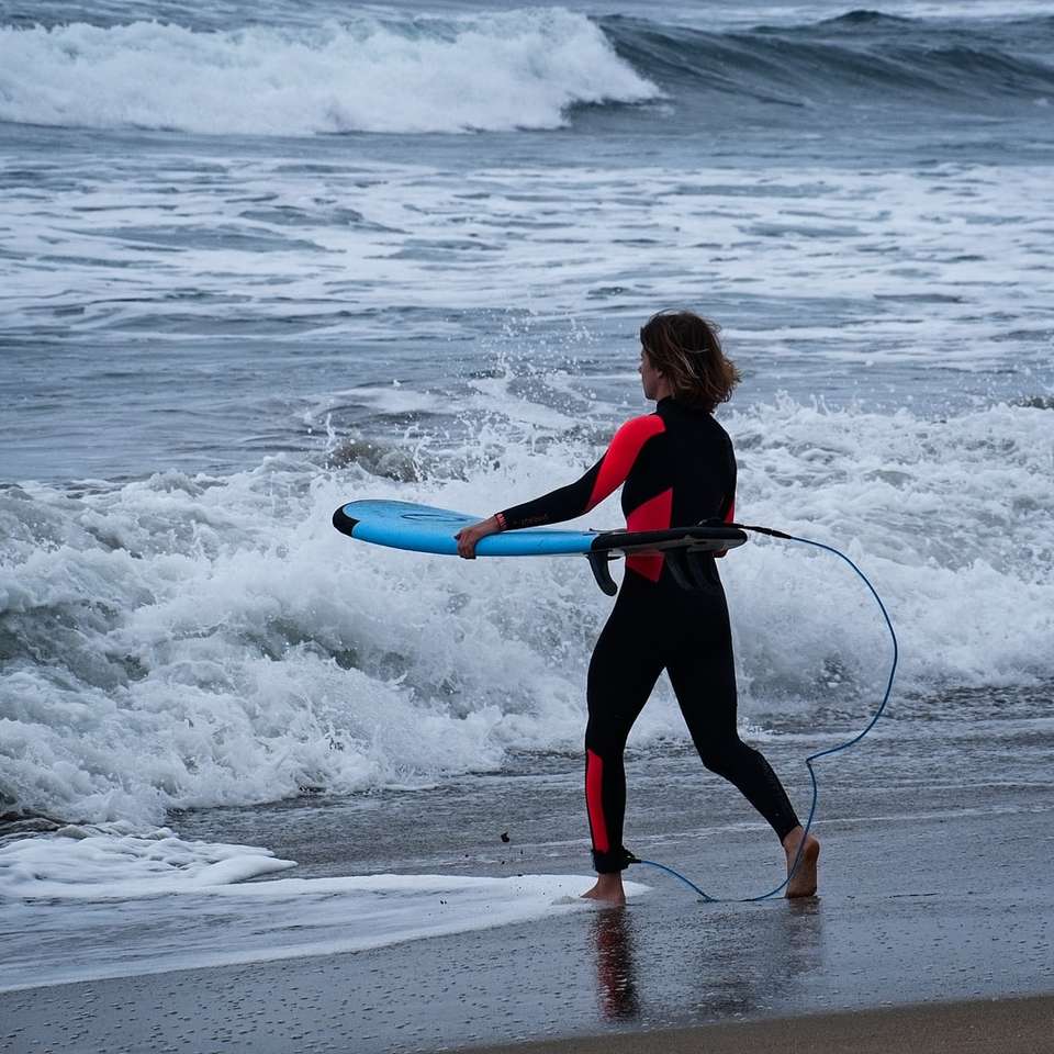 mulher de jaqueta preta e vermelha segurando uma prancha de surf azul puzzle online