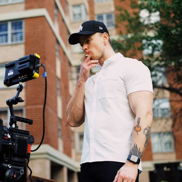 férfi fehér ingben és fekete rövidnadrágban, kezében fekete kamerával online puzzle