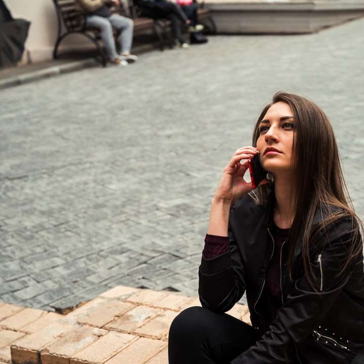 kobieta w czarnej skórzanej kurtce siedząca na brązowej ceglanej podłodze puzzle przesuwne online