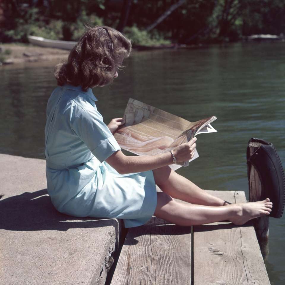 Frau mit blauem Kleid liest Zeitschrift in der Nähe des Körpers Online-Puzzle