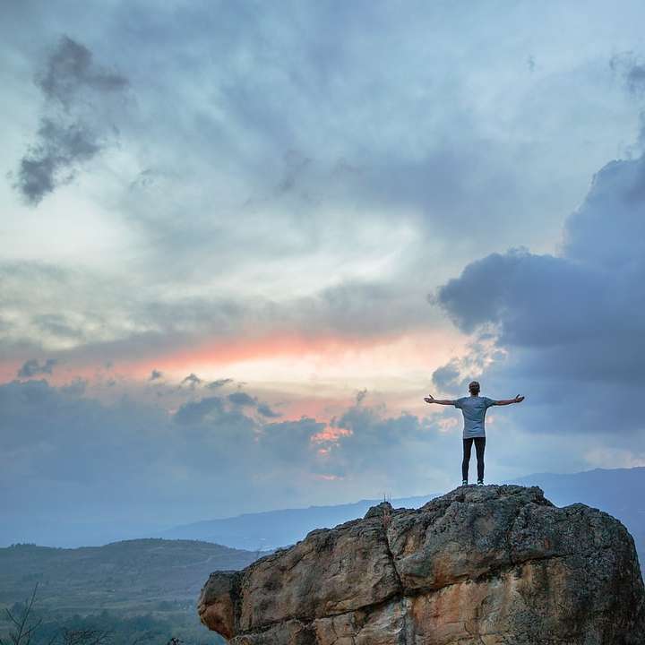 uomo in piedi sulla cima di una montagna rocciosa durante l'ora d'oro puzzle scorrevole online