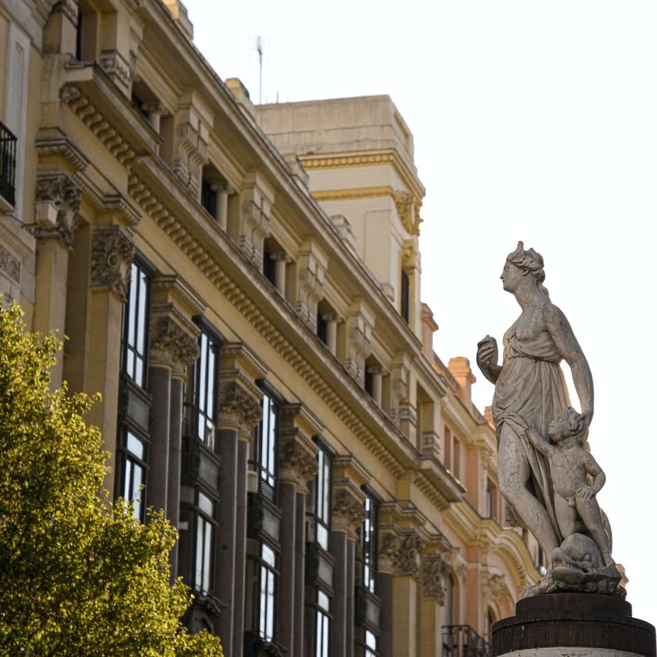 Estatua del hombre delante del edificio de hormigón beige puzzle deslizante online