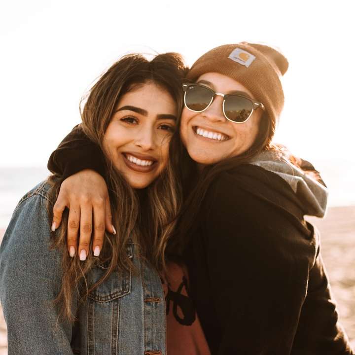 Mujer abrazando a otra mujer mientras sonríe en la playa rompecabezas en línea