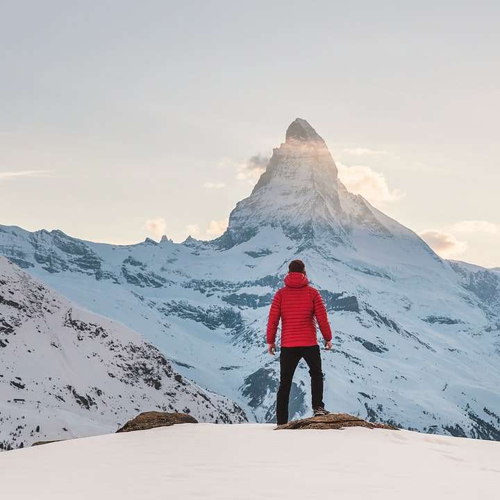 Persona con sudadera roja de pie en la montaña nevada puzzle deslizante online