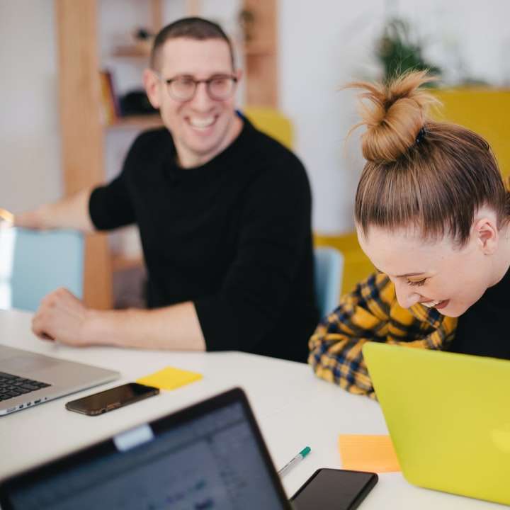 hombre y mujer riendo mientras está sentado frente a computadoras portátiles rompecabezas en línea