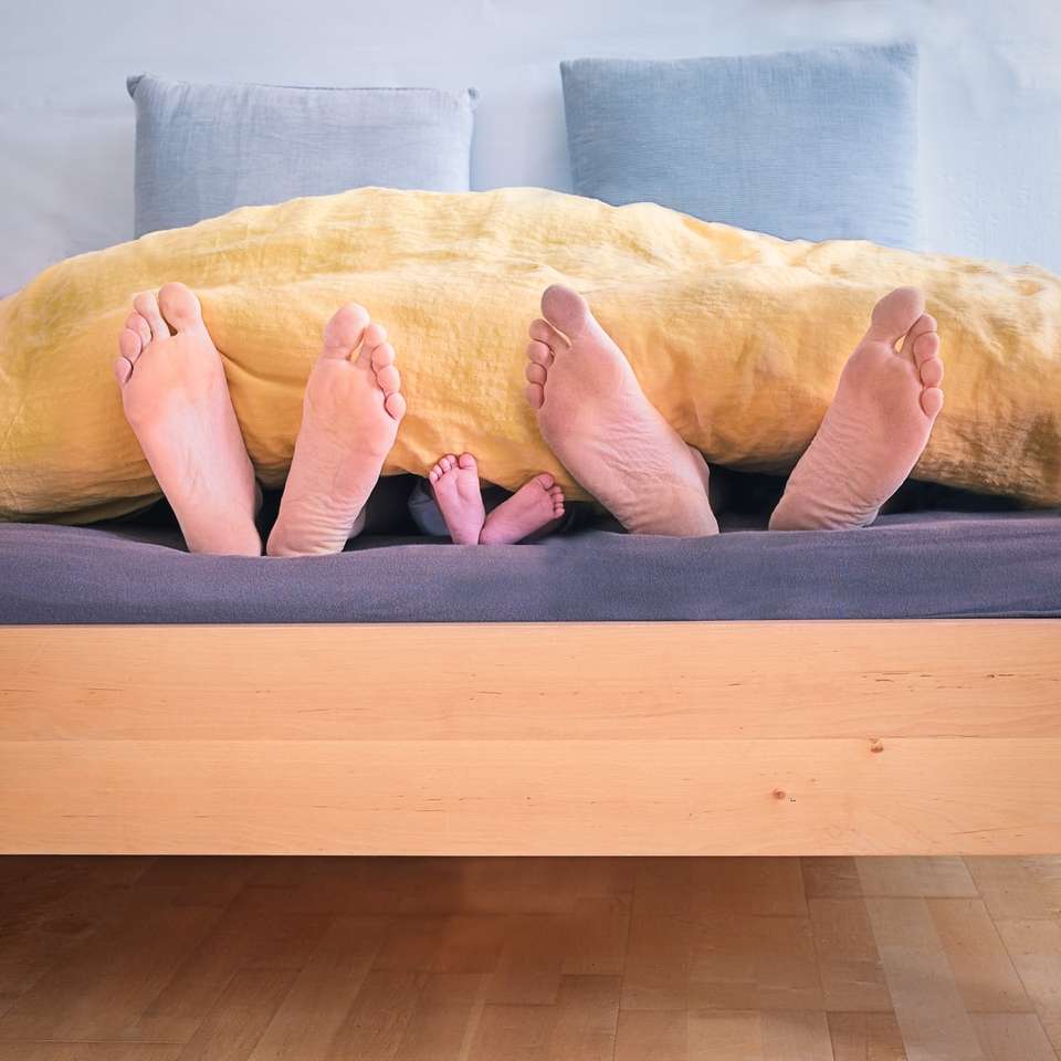 τρία άτομα κάτω από την κίτρινη κουβέρτα κρεβατιού συρόμενο παζλ online