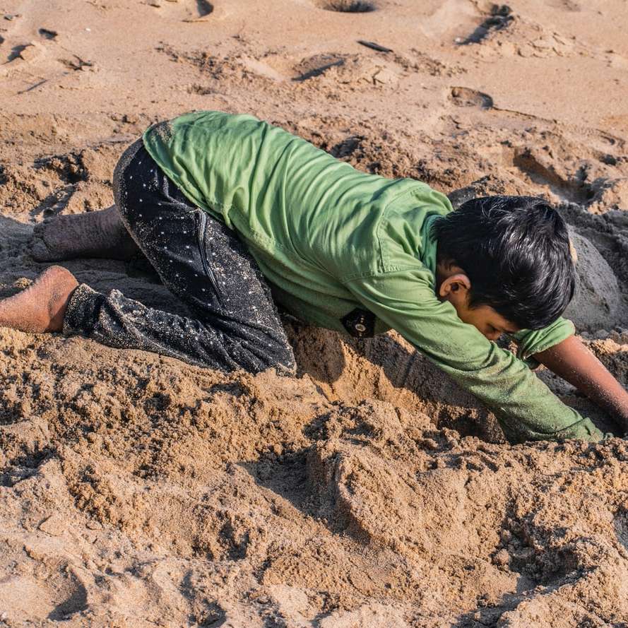 férfi zöld ingben és fekete nadrágban ül a barna homokon online puzzle