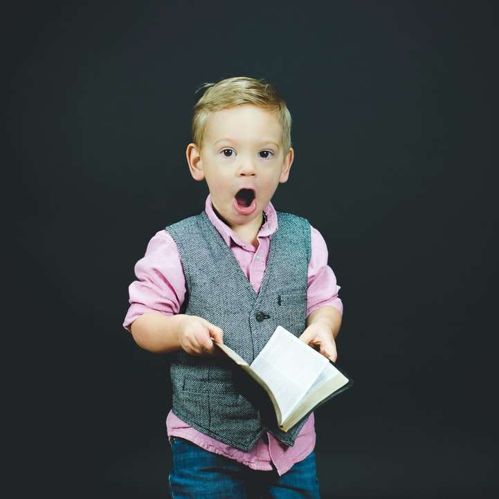 boy wearing gray vest and pink dress shirt holding book online puzzle