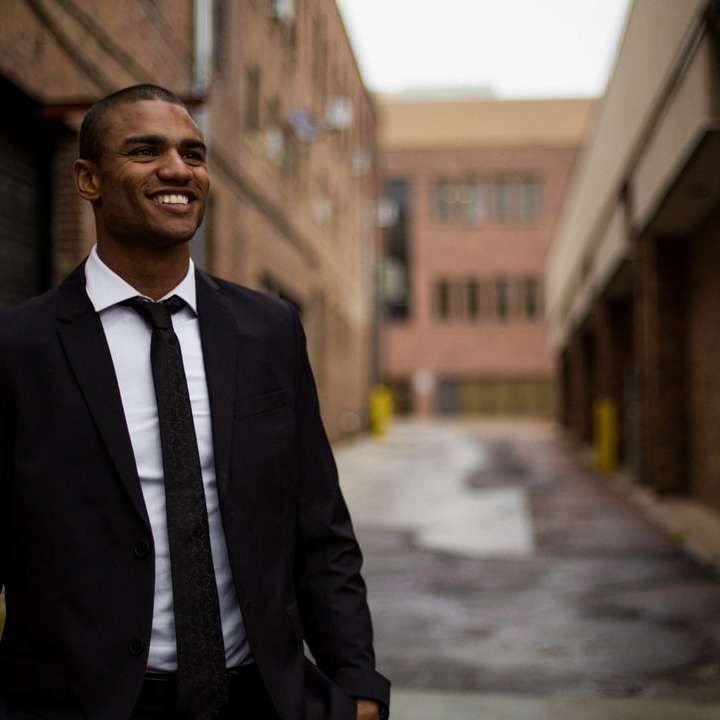 usmívající se muž stojící mezi hnědými betonovými budovami posuvné puzzle online