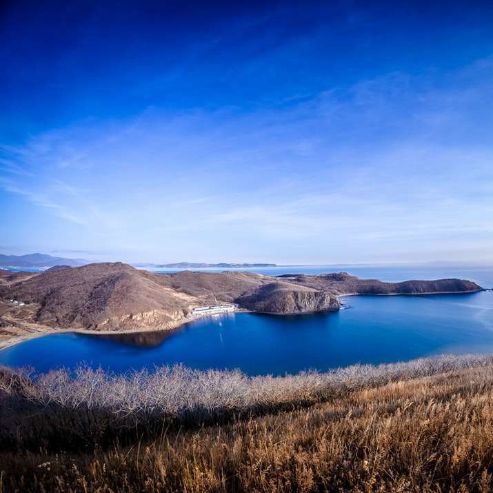 barna füves területen kék tó közelében, kék ég alatt online puzzle