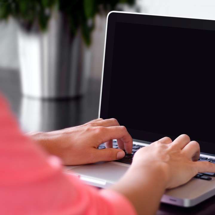 person wearing pink shirt typing on gray laptop computer sliding puzzle online
