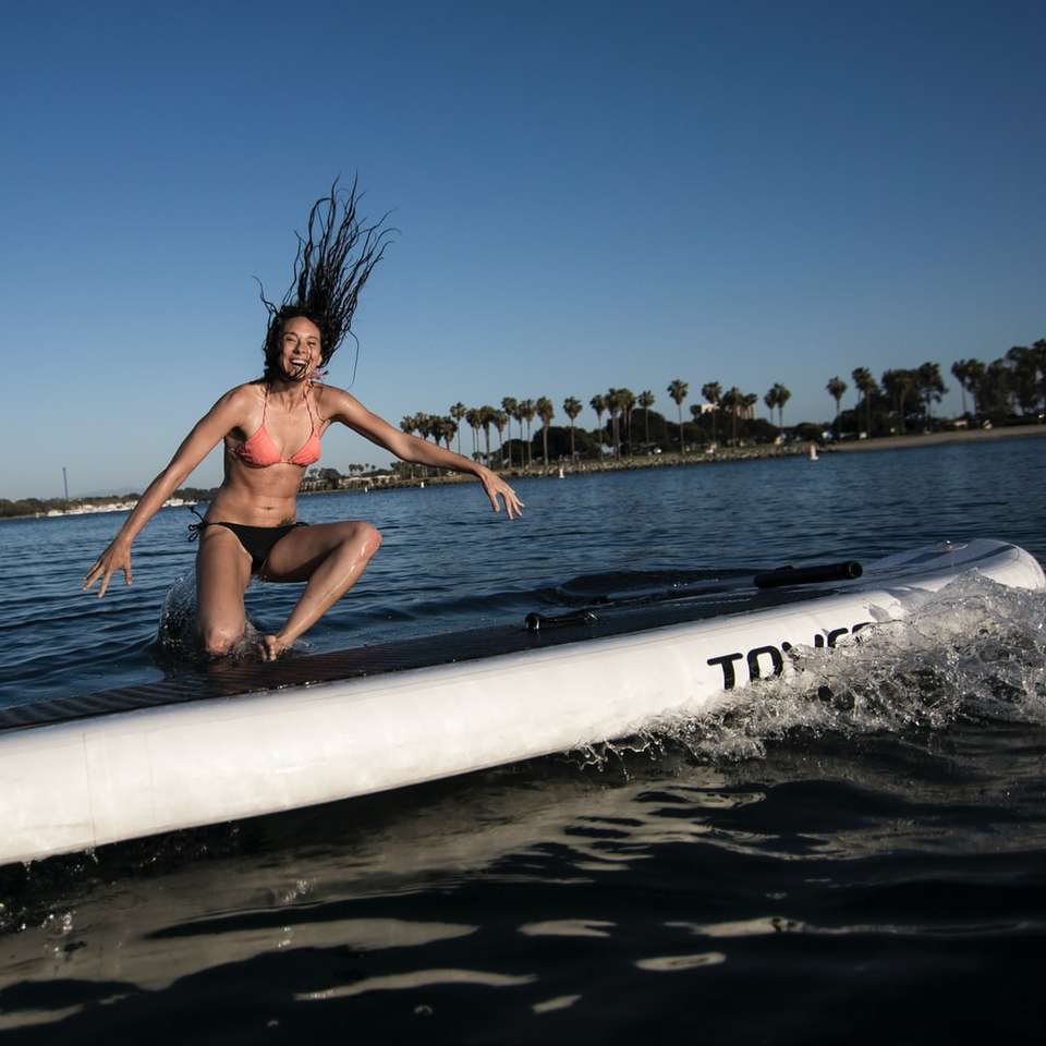 kobieta w niebieskim bikini leżąca na białej desce surfingowej na morzu puzzle online
