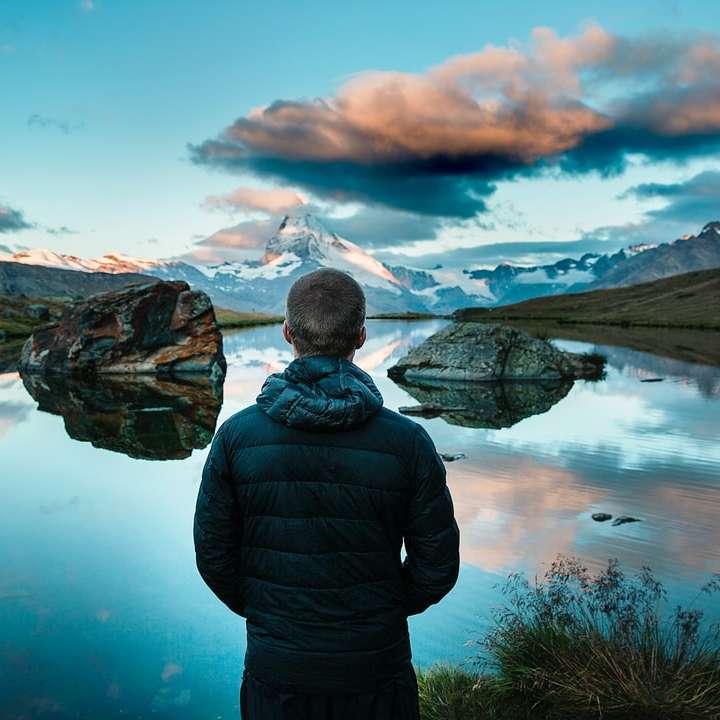 uomo in piedi di fronte al lago circondato da montagne puzzle online