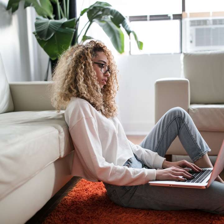 γυναίκα κάθεται στο πάτωμα και ακουμπά στον καναπέ χρησιμοποιώντας φορητό υπολογιστή συρόμενο παζλ online
