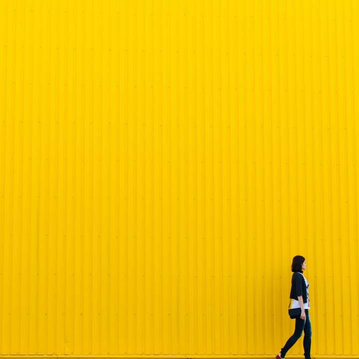 жінка в чорному топі стоїть біля жовтої стіни онлайн пазл
