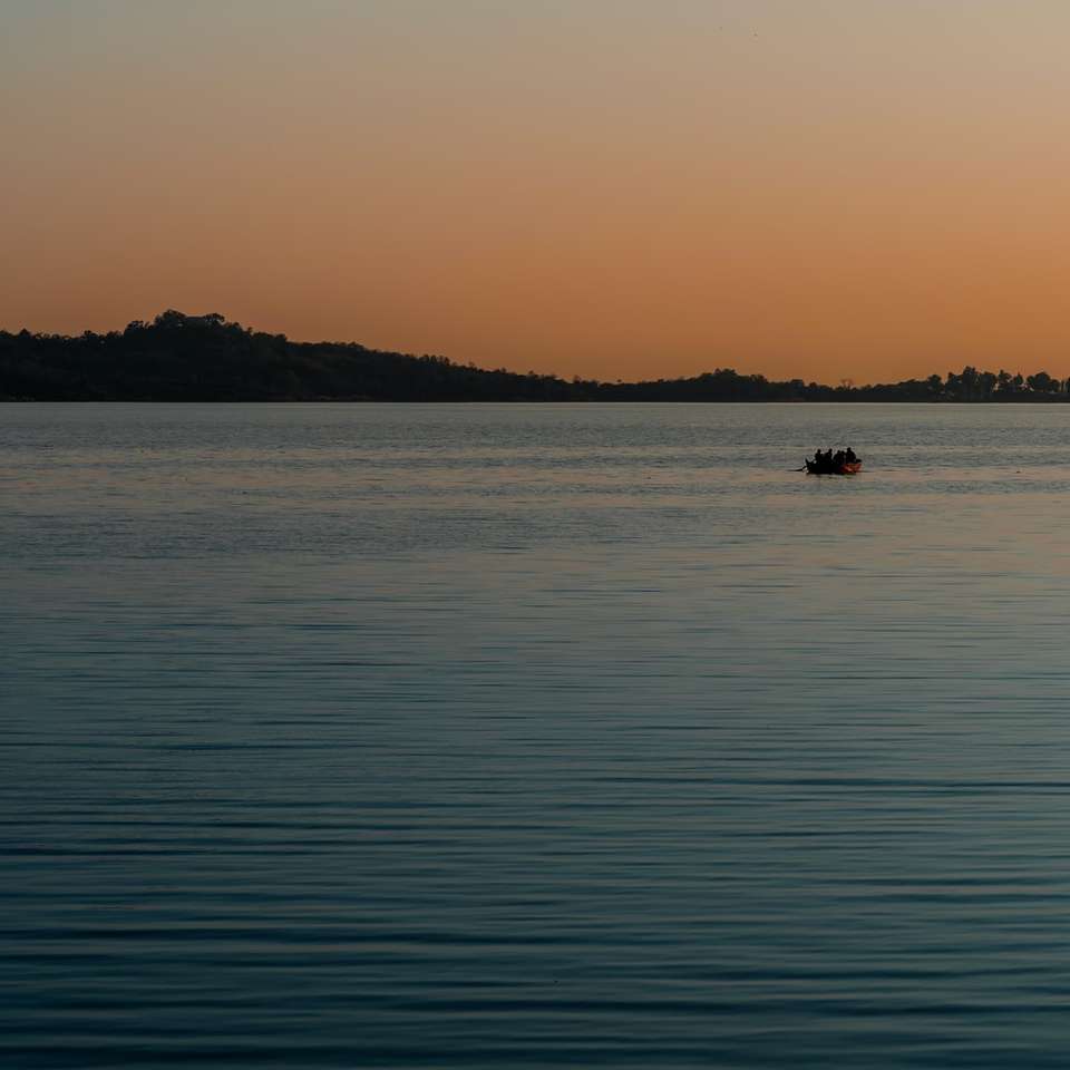 silhuett av person som åker båt på havet under solnedgången glidande pussel online