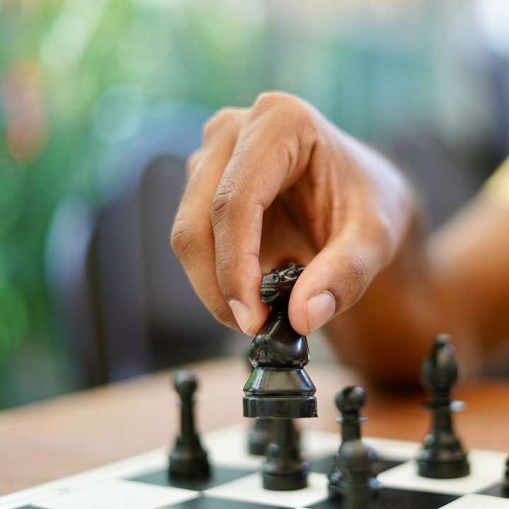 person holding black and silver chess piece sliding puzzle online